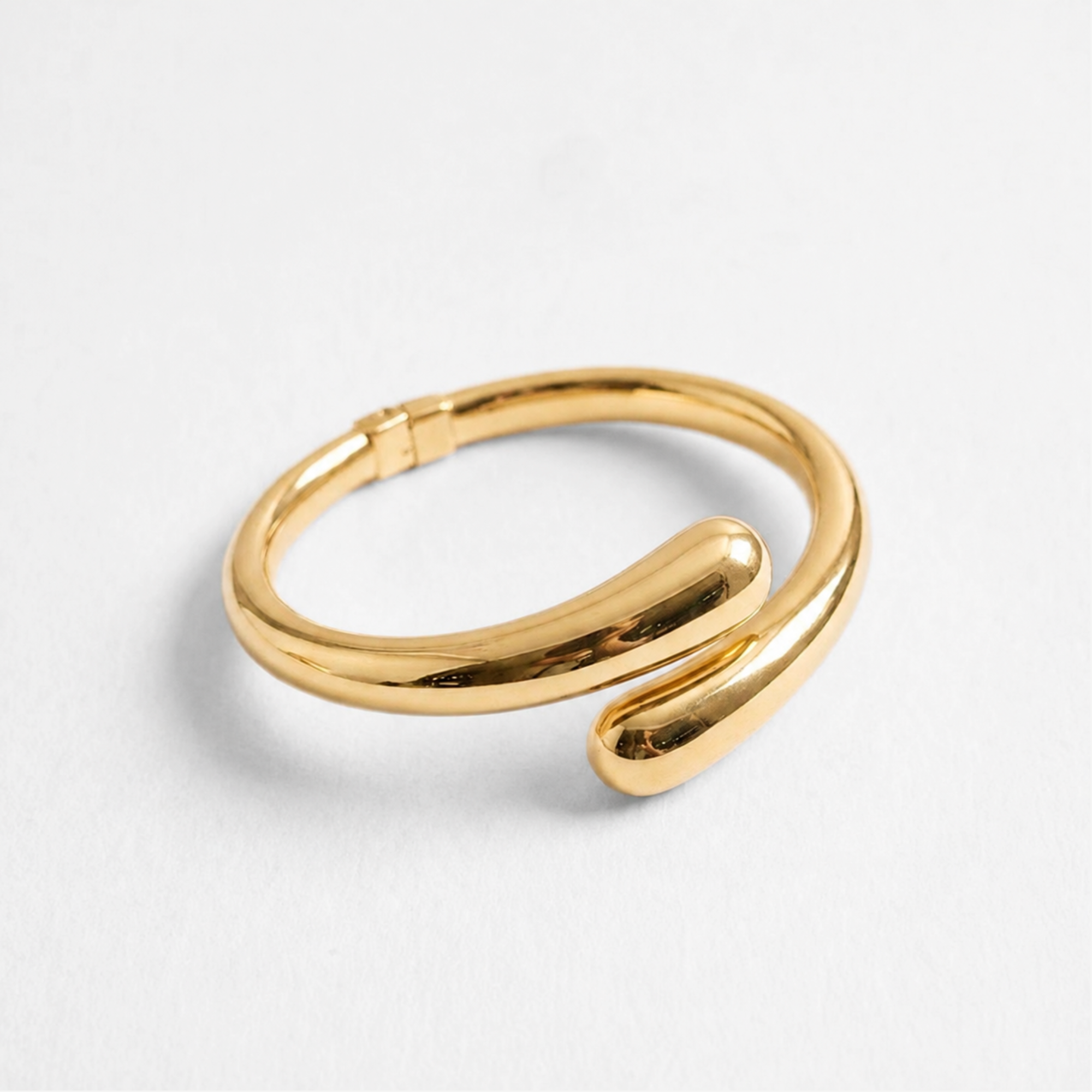 Modern gold open cuff bangle bracelet with sculptural rounded ends and a high-shine polished finish, photographed on a white background.