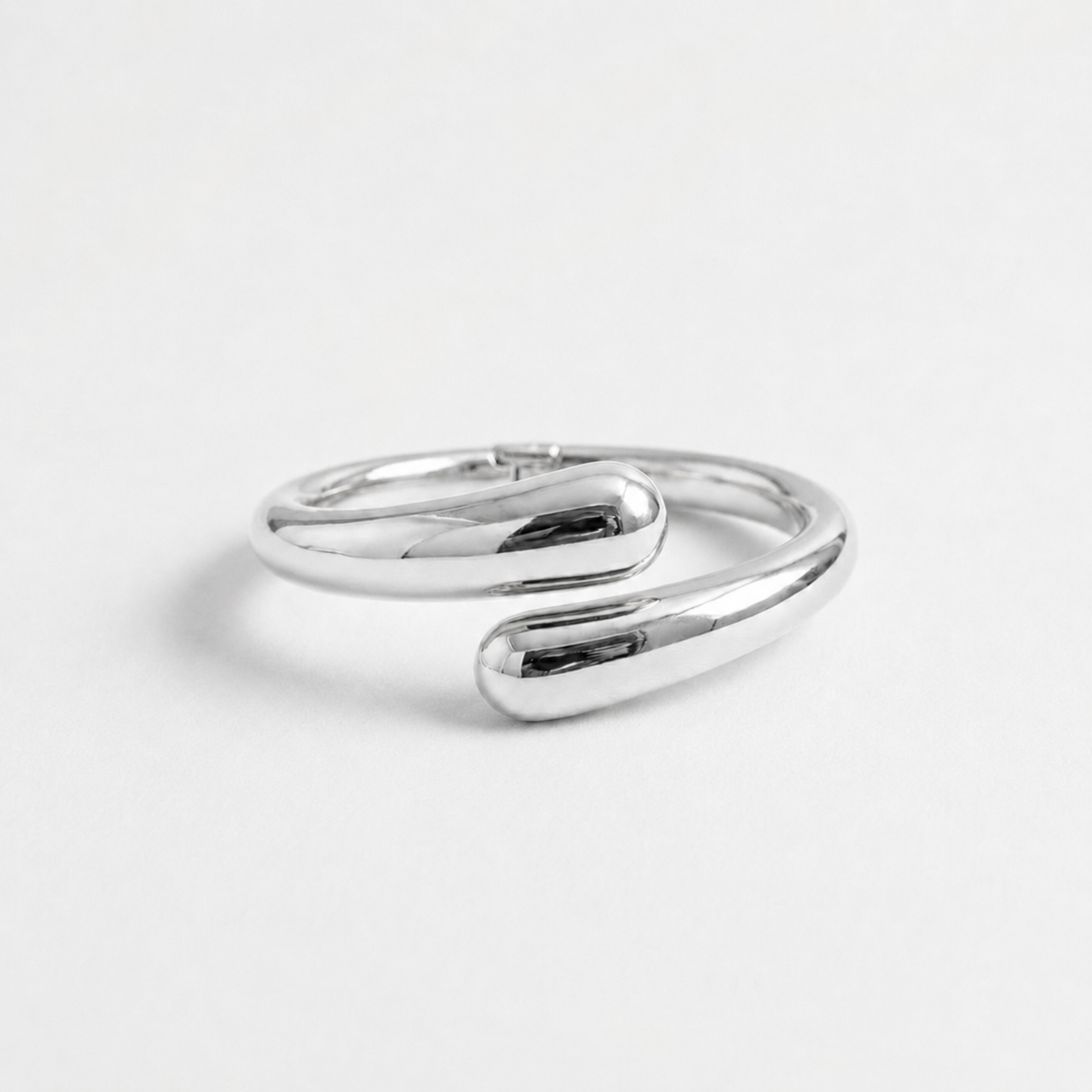 Silver open cuff bangle bracelet for women with a polished sculptural design and rounded teardrop ends, photographed on a clean white background.
