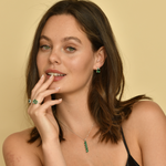 Woman wearing emerald jewelry set; emerald pendant in baguette cut, multi stone emerald rings, and green emerald stud earrings.