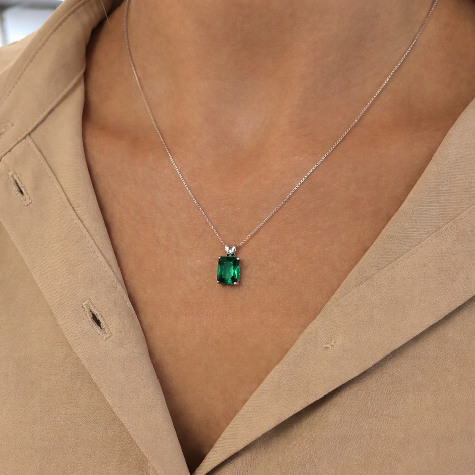Necklace with a green gemstone pendant worn by a person in a beige coat.